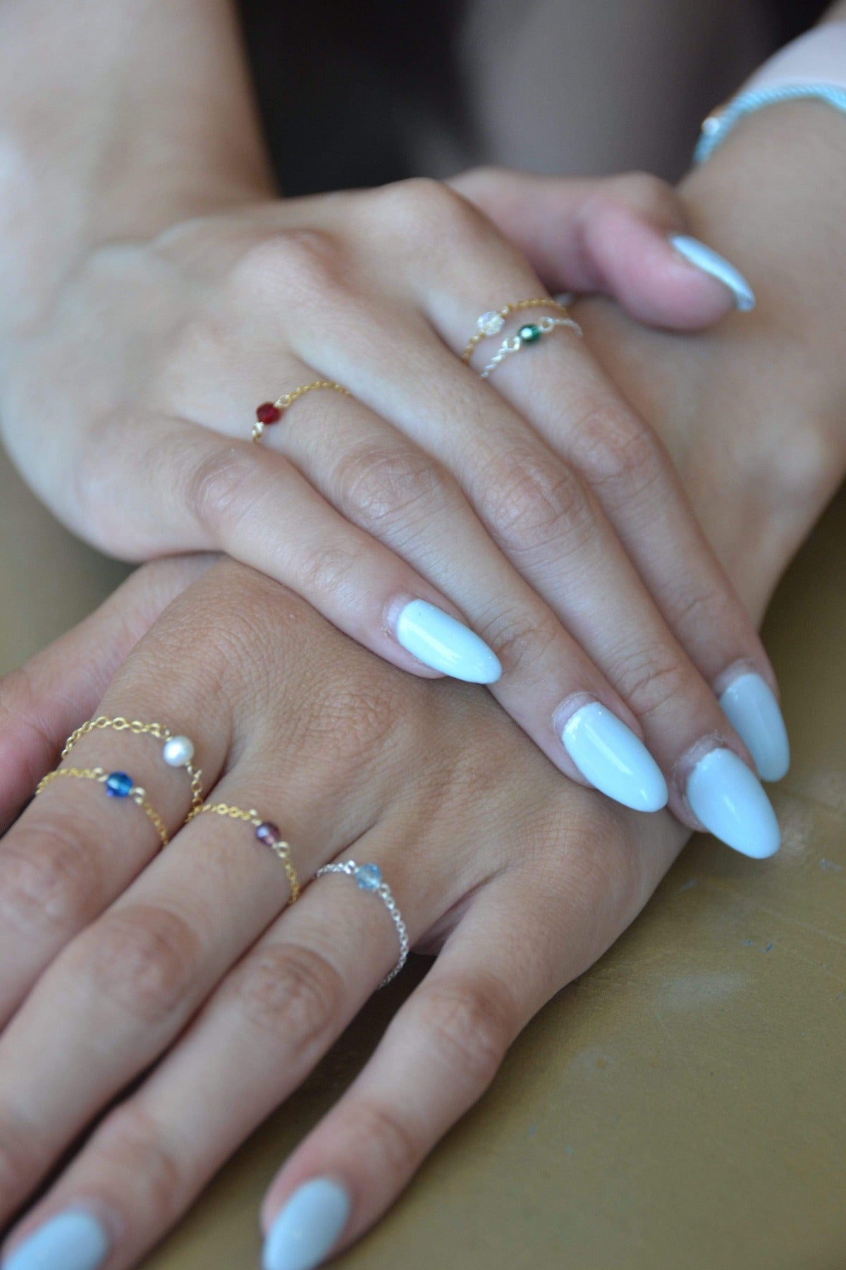 gold and silver birthstone chain rings on both hands of model