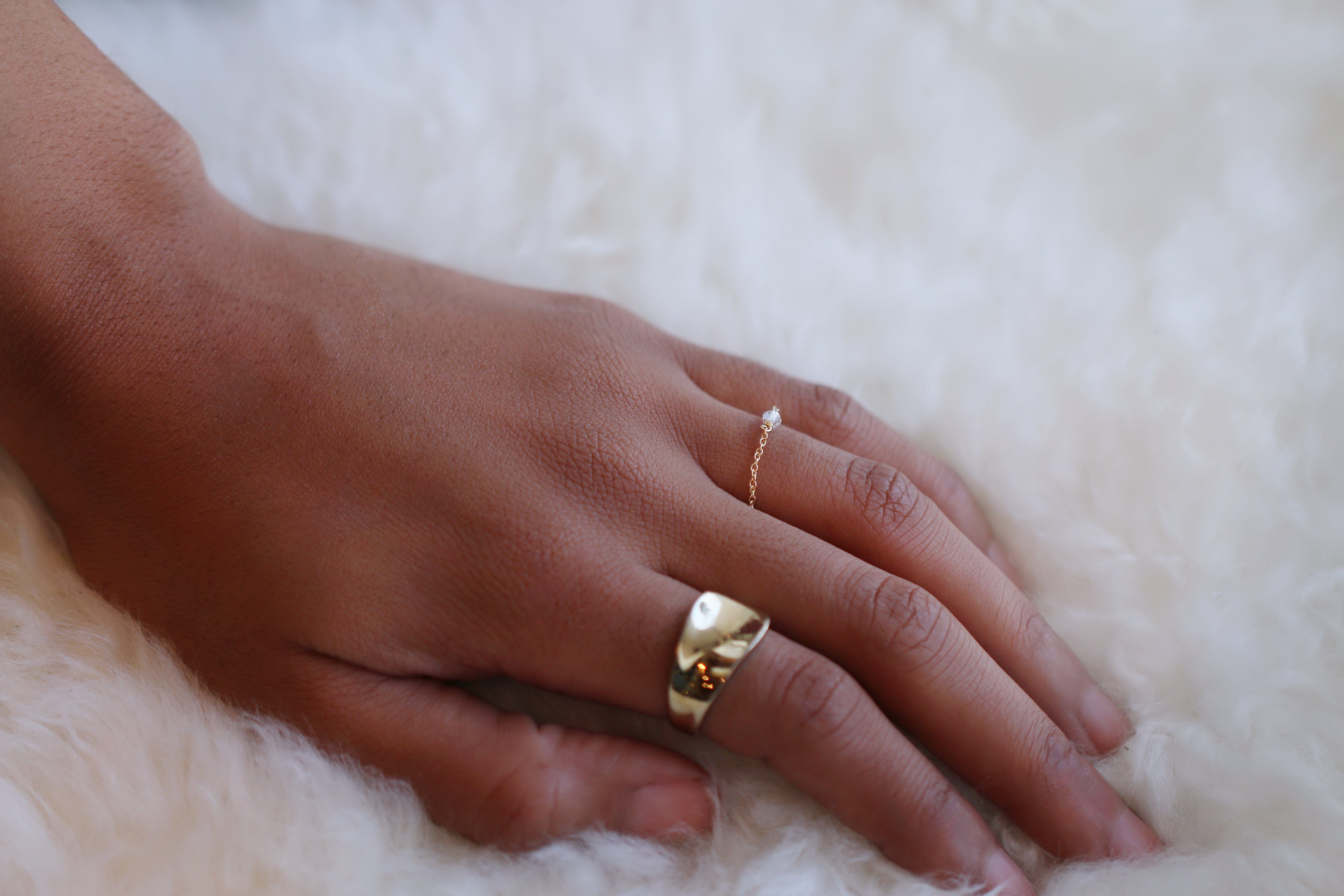 Close up picture of a model's hand wearing a gold statement ring and a dainty chain ring - MaeMae Jewelry