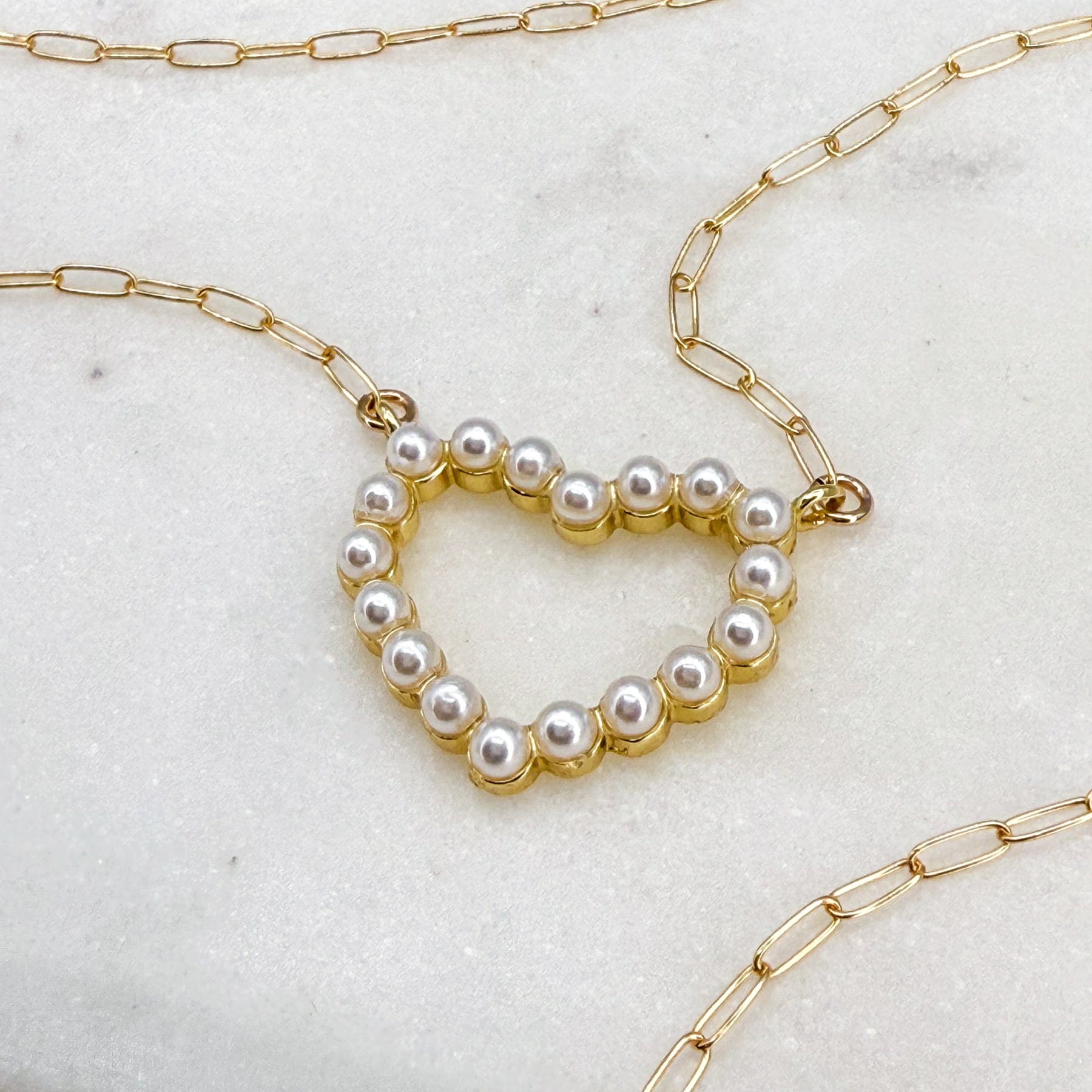 Heart-shaped dainty pearl necklace on a marble slate background, on a 14k gold-filled paper clip chain by MaeMae Jewelry that is hypoallergenic and lead-free